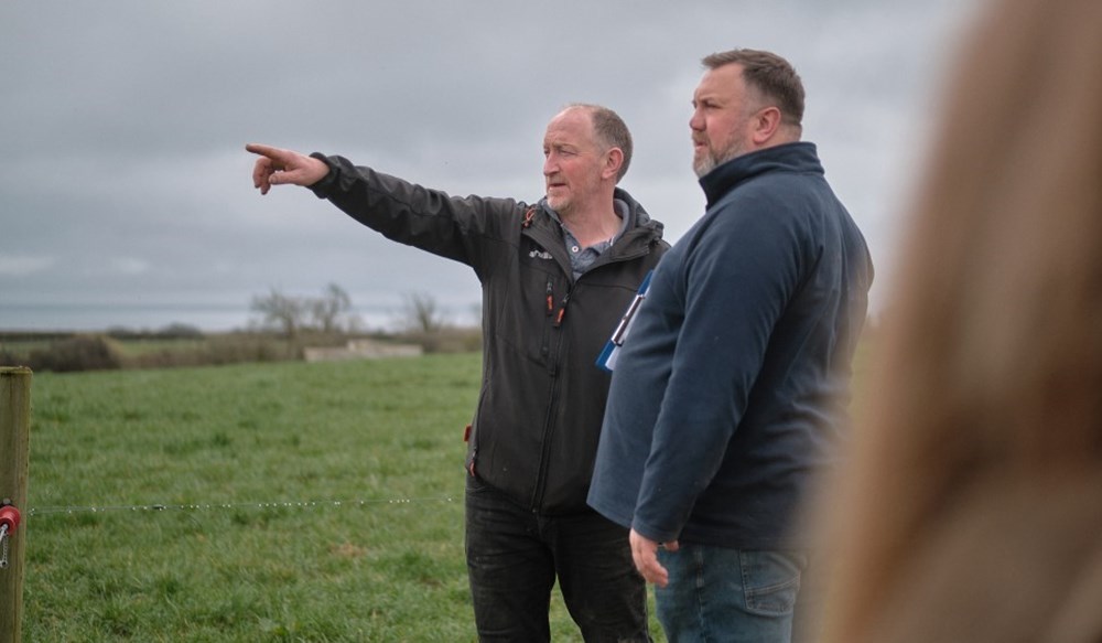 A man in a field pointing out something to another man